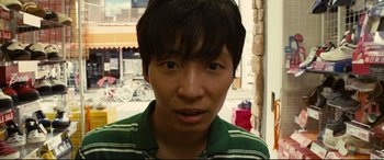 Movie still from “Why Don't You Play in Hell?” (2013), directed by Sion Sono – A young man with black hair wearing a green and white striped shirt; Close Up shot, High angle
