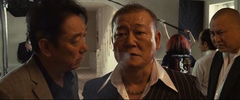 Movie still from “Why Don't You Play in Hell?” (2013), directed by Sion Sono – A man smoking a cigarette while another man looks on; Close Up shot, Low angle