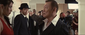 Movie still from “Why Don't You Play in Hell?” (2013), directed by Sion Sono – A group of men standing around each other in a room; Medium shot, Over the shoulder angle