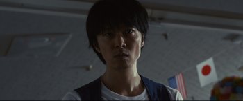 Movie still from “Why Don't You Play in Hell?” (2013), directed by Sion Sono – A man with a black hair and a white t - shirt; Close Up shot, Low angle