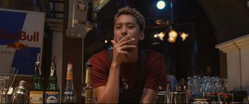 Movie still from “Why Don't You Play in Hell?” (2013), directed by Sion Sono – A man sitting at a table with a cigarette in his mouth; Medium shot, Low angle