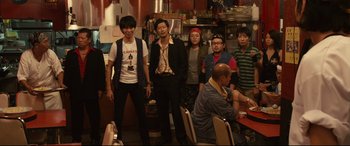Movie still from “Why Don't You Play in Hell?” (2013), directed by Sion Sono – A group of people standing around in a restaurant; Medium shot, Low angle