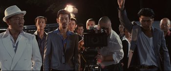 Movie still from “Why Don't You Play in Hell?” (2013), directed by Sion Sono – A group of people standing around a camera; Medium shot, Over the shoulder angle