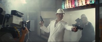 Movie still from “Why Don't You Play in Hell?” (2013), directed by Sion Sono – A man in a white suit and hat holding a gun; Medium shot, Low angle