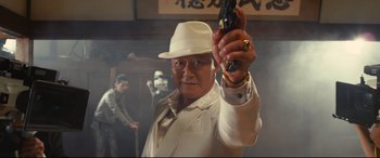 Movie still from “Why Don't You Play in Hell?” (2013), directed by Sion Sono – An older man in a white hat holding a gun; Medium shot, Low angle