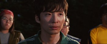 Movie still from “Why Don't You Play in Hell?” (2013), directed by Sion Sono – A young man with short black hair wearing a green shirt; Close Up shot, Low angle