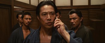 Movie still from “Why Don't You Play in Hell?” (2013), directed by Sion Sono – A man in a robe talking on a cell phone; Close Up shot, Low angle