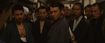 Movie still from “Why Don't You Play in Hell?” (2013), directed by Sion Sono – A group of men standing next to each other in a room; Medium shot, Low angle