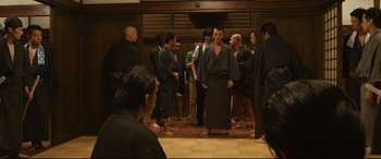 Movie still from “Why Don't You Play in Hell?” (2013), directed by Sion Sono – A group of people standing around a room; Wide shot, High angle