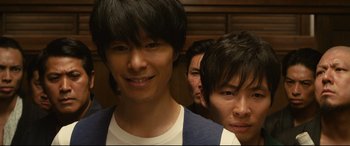 Movie still from “Why Don't You Play in Hell?” (2013), directed by Sion Sono – A group of young men standing next to each other in a room; Close Up shot, Low angle