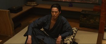 Movie still from “Why Don't You Play in Hell?” (2013), directed by Sion Sono – A man sitting on the ground wearing a robe; Medium shot, High angle