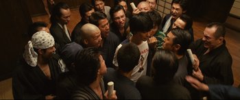 Movie still from “Why Don't You Play in Hell?” (2013), directed by Sion Sono – A group of people standing around each other in a room; Medium shot, High angle