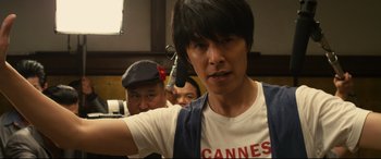 Movie still from “Why Don't You Play in Hell?” (2013), directed by Sion Sono – A man in a white t - shirt is looking at the camera; Close Up shot, Low angle