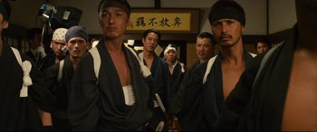 Movie still from “Why Don't You Play in Hell?” (2013), directed by Sion Sono – A group of men standing next to each other; Medium shot, Low angle