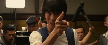 Movie still from “Why Don't You Play in Hell?” (2013), directed by Sion Sono – A young man pointing to the camera while wearing a white t - shirt; Close Up shot, Low angle