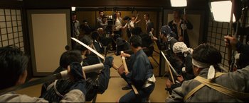 Movie still from “Why Don't You Play in Hell?” (2013), directed by Sion Sono – A group of people in a room holding swords; Wide shot, High angle