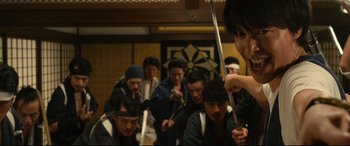 Movie still from “Why Don't You Play in Hell?” (2013), directed by Sion Sono – A group of people in a room holding swords; Medium shot, Low angle