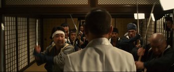 Movie still from “Why Don't You Play in Hell?” (2013), directed by Sion Sono – A group of people in a room holding swords; Medium shot, Over the shoulder angle