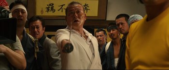 Movie still from “Why Don't You Play in Hell?” (2013), directed by Sion Sono – A man in a white suit is holding a whip; Medium shot, Low angle