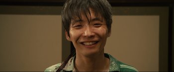 Movie still from “Why Don't You Play in Hell?” (2013), directed by Sion Sono – A young man smiling for the camera; Close Up shot, High angle