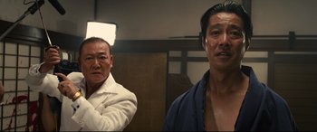 Movie still from “Why Don't You Play in Hell?” (2013), directed by Sion Sono – Two asian men standing next to each other in a room; Medium shot, Low angle