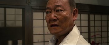 Movie still from “Why Don't You Play in Hell?” (2013), directed by Sion Sono – An older man wearing a white dress shirt and tie; Close Up shot, Low angle