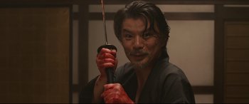 Movie still from “Why Don't You Play in Hell?” (2013), directed by Sion Sono – A man holding a sword in his hand; Close Up shot, Low angle