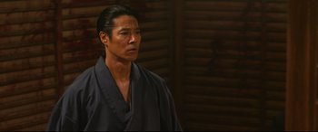 Movie still from “Why Don't You Play in Hell?” (2013), directed by Sion Sono – A man in a robe stands in front of a wooden wall; Close Up shot, Low angle