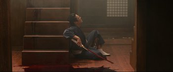 Movie still from “Why Don't You Play in Hell?” (2013), directed by Sion Sono – A man sitting on the ground holding an umbrella; Wide shot, High angle