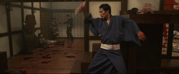Movie still from “Why Don't You Play in Hell?” (2013), directed by Sion Sono – A man in a blue robe is holding a sword; Wide shot, Low angle