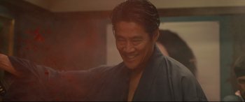 Movie still from “Why Don't You Play in Hell?” (2013), directed by Sion Sono – A person wearing a robe smiling; Medium shot, Low angle