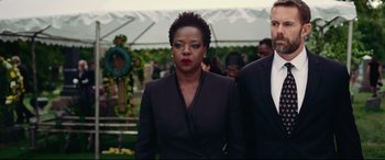 Movie still from “Widows” (2018), directed by Steve McQueen – A woman in a black suit standing next to a man in a black suit; Medium shot, Over the shoulder angle