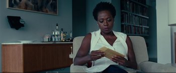 Movie still from “Widows” (2018), directed by Steve McQueen – A woman sitting in a chair looking at a piece of paper; Medium shot, Over the shoulder angle