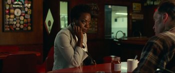 Movie still from “Widows” (2018), directed by Steve McQueen – A woman sitting at a table in a restaurant talking on the phone; Medium shot, Over the shoulder angle