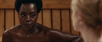 Movie still from “Widows” (2018), directed by Steve McQueen – A woman sitting on a wooden bench in front of a wooden wall; Close Up shot, Over the shoulder angle