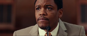 Movie still from “Widows” (2018), directed by Steve McQueen – A person wearing a suit and tie; Close Up shot, High angle