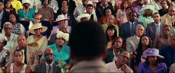 Movie still from “Widows” (2018), directed by Steve McQueen – A crowd of people sitting in a room; Close Up shot, Over the shoulder angle