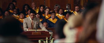 Movie still from “Widows” (2018), directed by Steve McQueen – A group of people sitting at a podium in front of microphones; Medium shot, Over the shoulder angle