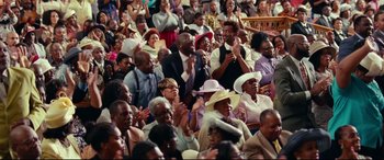 Movie still from “Widows” (2018), directed by Steve McQueen – A group of people sitting in a room clapping; Medium shot, High angle