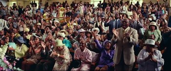 Movie still from “Widows” (2018), directed by Steve McQueen – A group of people sitting and standing in a room; Wide shot, High angle