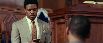 Movie still from “Widows” (2018), directed by Steve McQueen – A man in a suit and tie looking at his cell phone; Close Up shot, Over the shoulder angle