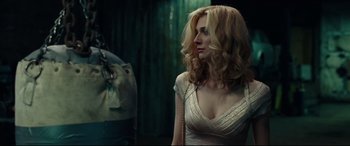 Movie still from “Widows” (2018), directed by Steve McQueen – A woman in a white dress is standing in front of a green curtain; Medium shot, Over the shoulder angle