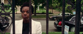 Movie still from “Widows” (2018), directed by Steve McQueen – A woman in a white jacket standing in front of a fence; Close Up shot, Over the shoulder angle