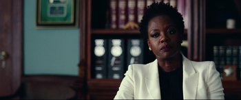 Movie still from “Widows” (2018), directed by Steve McQueen – A woman in a white jacket sitting in front of a book case; Close Up shot, Over the shoulder angle