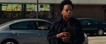 Movie still from “Widows” (2018), directed by Steve McQueen – A woman in a black jacket is holding a cell phone; Medium shot, Over the shoulder angle