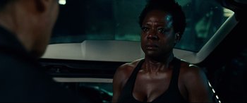 Movie still from “Widows” (2018), directed by Steve McQueen – A woman in a black tank top is standing in front of a car; Close Up shot, Over the shoulder angle