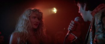 Movie still from “Wild at Heart” (1990), directed by David Lynch – A woman with long blonde curly hair holding a microphone; Close Up shot, Over the shoulder angle