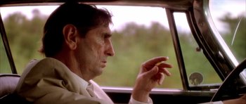Movie still from “Wild at Heart” (1990), directed by David Lynch – A man sitting in the back seat of a car holding something; Close Up shot, Over the shoulder angle