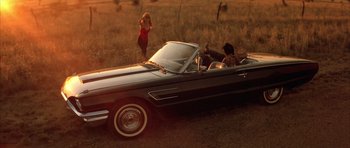 Movie still from “Wild at Heart” (1990), directed by David Lynch – A woman in a red dress standing next to an old car; Wide shot, High angle