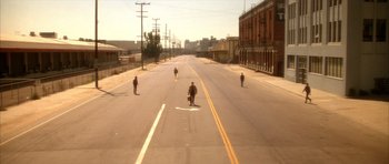 Movie still from “Wild at Heart” (1990), directed by David Lynch – A group of skateboarders riding down the middle of an empty street; Extreme Wide shot, High angle